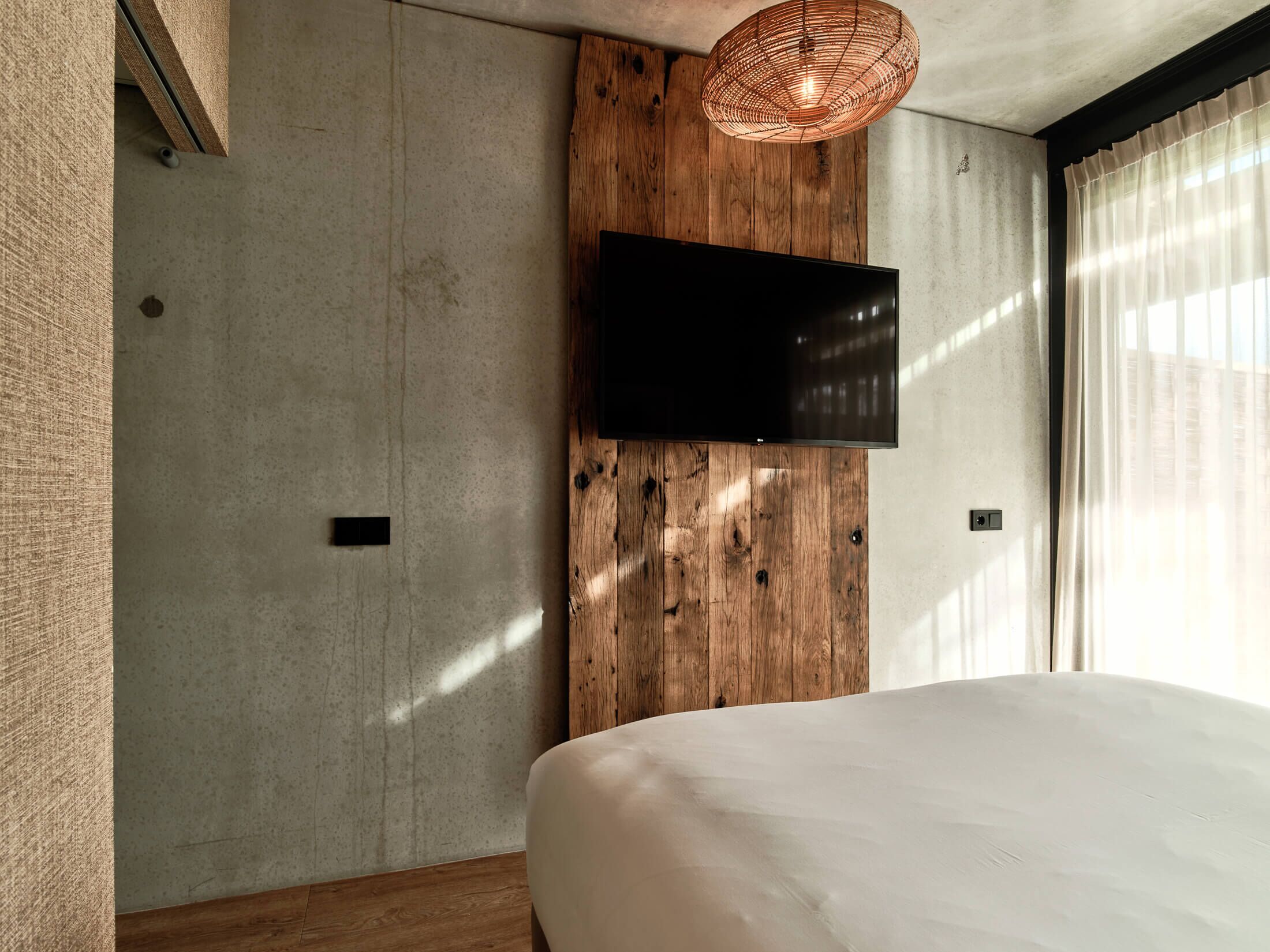 A modern bedroom with a large bed, a mounted TV, and a wooden accent wall.