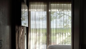 Un dormitorio con cama, suelo de madera y un ventanal con cortinas translúcidas.