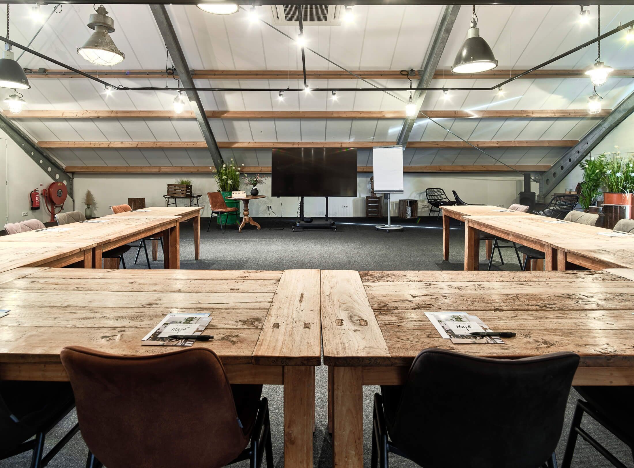 Une salle de conférence avec de longues tables en bois, des chaises noires et un grand écran.