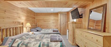 A wooden cabin room with two beds, a dresser, a TV, and a door leading outside.