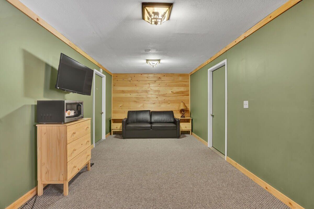 A small, cozy room with a wooden ceiling, a flat-screen TV, a black leather sofa, and a wooden dresser.