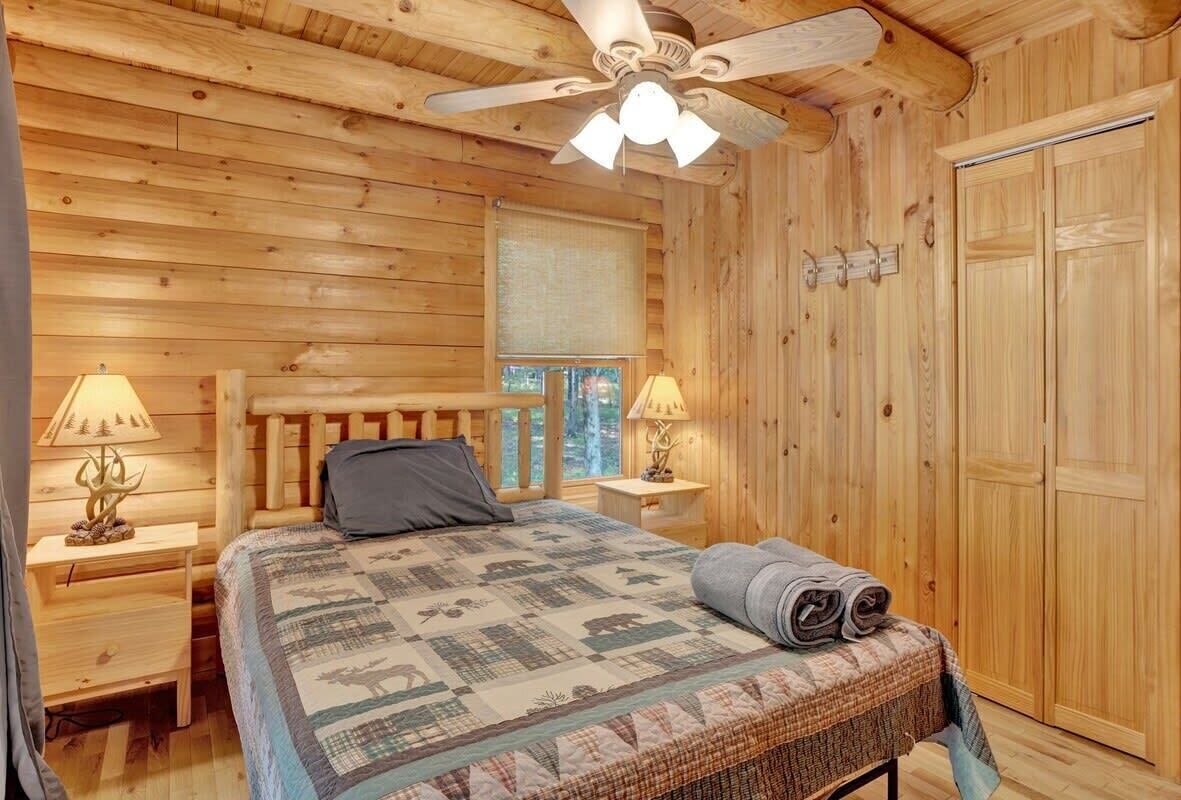 Ein Schlafzimmer einer Holzhütte mit einem Bett, zwei Nachttischen, einem Deckenventilator und einem Kleiderschrank.
