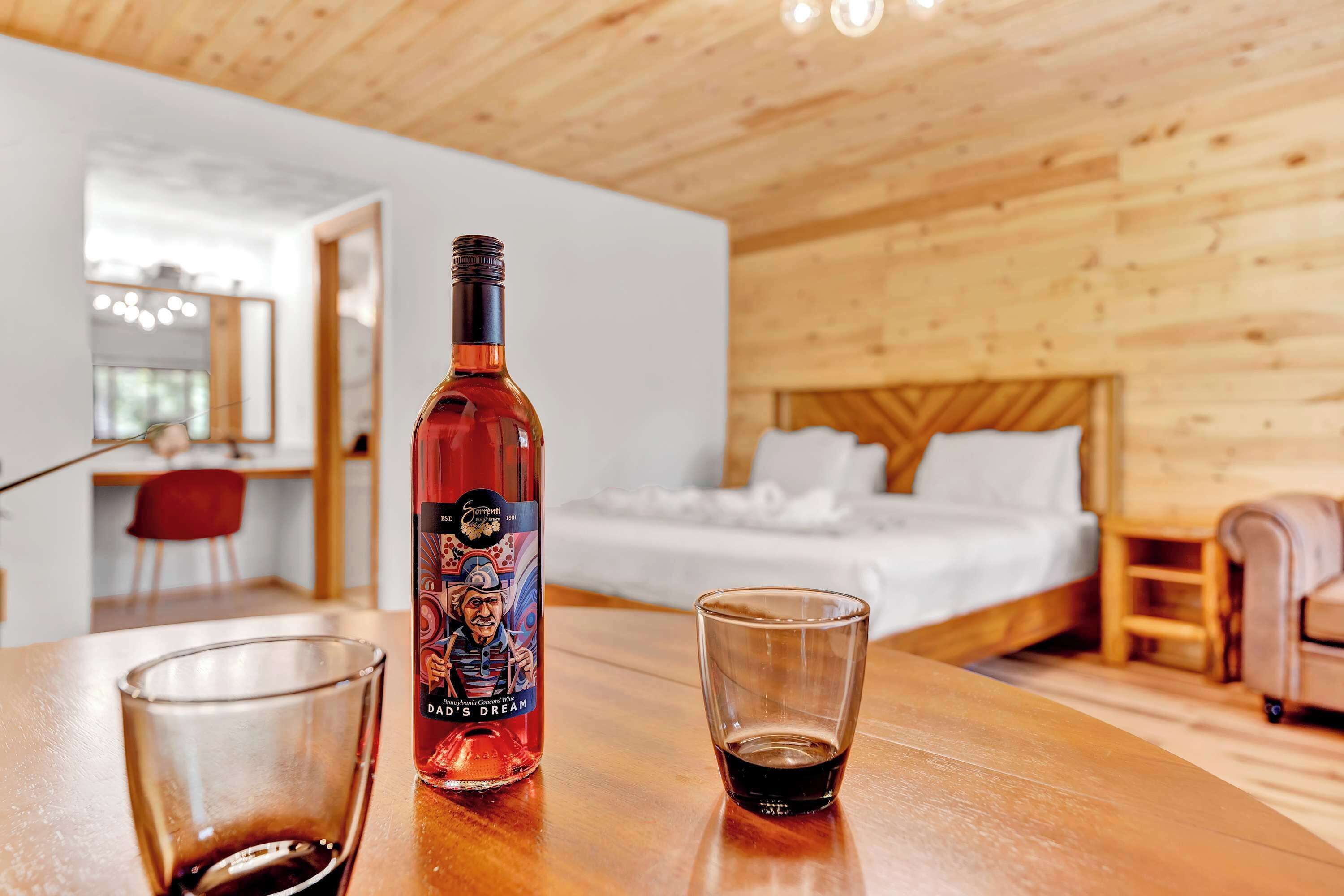 A wooden interior with a bed, a table with a bottle and a glass, and a mirror in the background.