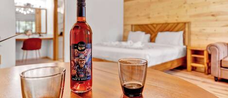 A wooden interior with a bed, a table with a bottle and a glass, and a mirror in the background.