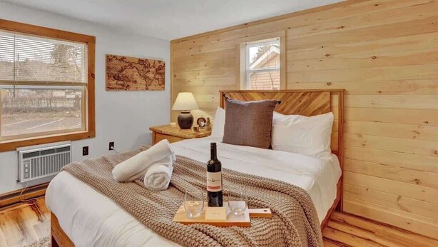 Ein gemütliches Schlafzimmer mit Holz-Kopfteil, einem Bett mit weißer Bettdecke, einer Weinflasche und einem Tablett mit Gläsern.