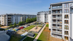 Ein moderner Apartmentkomplex mit mehreren Etagen, Balkonen und einem Parkplatz.