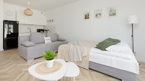 Ein modernes Wohnzimmer mit einem grauen Sofa, einem weißen Bett und einem kleinen, weißen Tisch mit einer Pflanze.