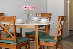 A dining table set with white plates, clear glassware, and pink flowers in a vase. - Sunny Studio in Warsaw | Balcony and Private Parking (Warszawa)