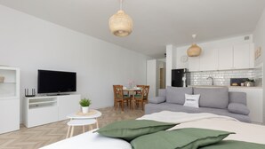 Ein modernes Wohnzimmer mit einer Couch, einem Fernseher, einem Esstisch mit Stühlen und einer Küchenzeile mit Spüle und Schränken.