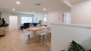 A spacious living area with a wooden dining table, white chairs, a blue sofa, and a large plant. - The Juni-7 Unit Renovated Complex (Cocoa Beach)