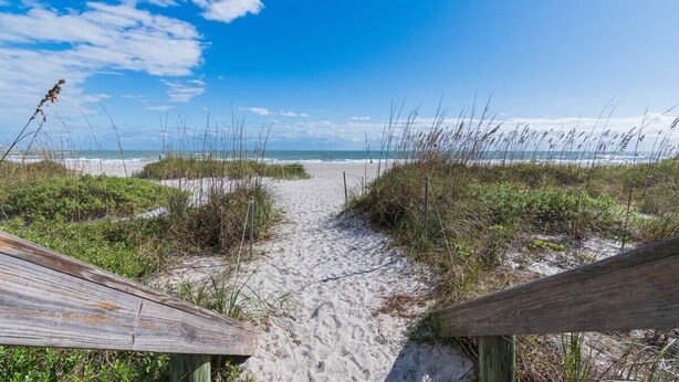 A sandy beach path leading to the ocean, surrounded by vegetation. - The Juni-7 Unit Renovated Complex (Cocoa Beach)