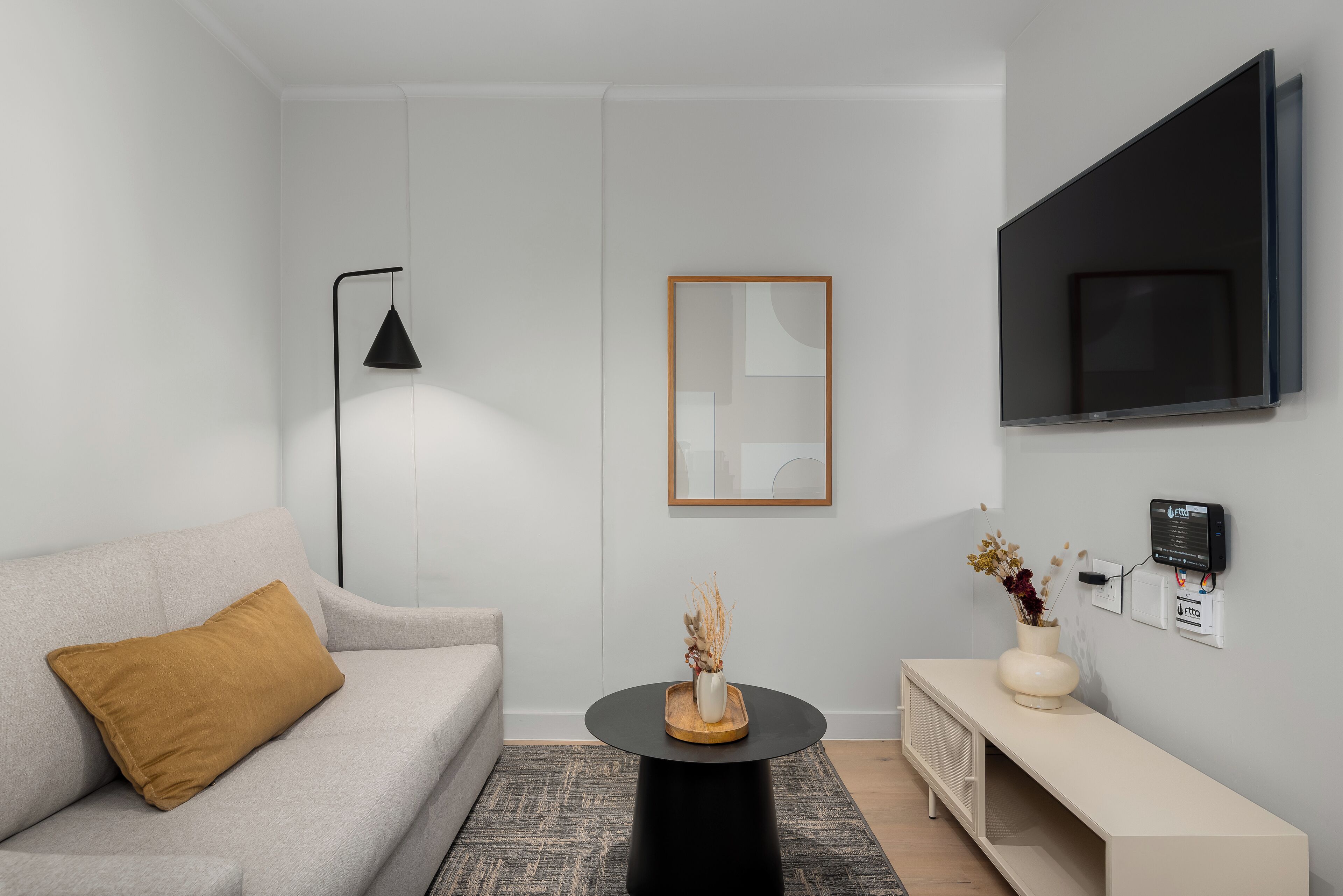 A modern living room with a sofa, a coffee table, a TV, and a wall-mounted control panel.