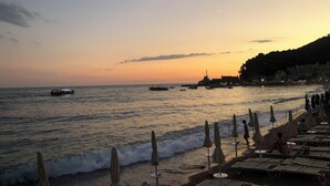 A beach with rows of sun loungers and umbrellas, a calm sea, and a sunset in the background.