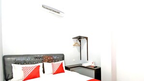 Een hotelkamer met een bed, nachtkastje, hanglamp en een wandairconditioner.