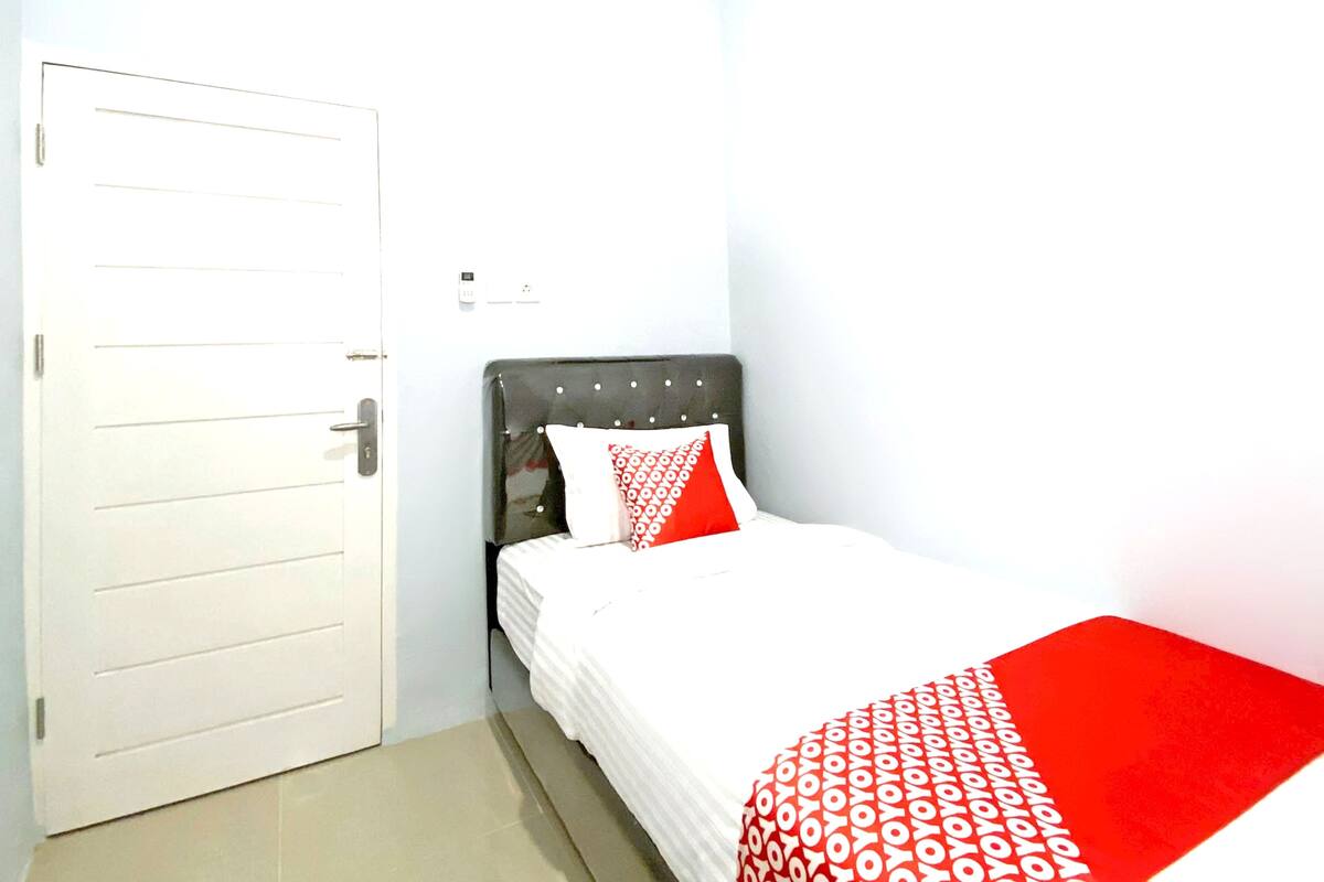 Une chambre avec une porte blanche, un lit recouvert d’une couvre-lit à motifs rouges et blancs, et une couverture rouge.