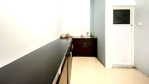 Een smalle, zwak verlichte gang met een donkere vloer, een kleine kitchenette met een spoelbak en kastjes, en een deur met een raam.