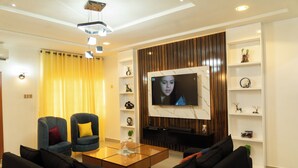 Een moderne woonkamer met een flatscreen-tv, twee fauteuils, een bank, een salontafel en decoratieve planken.