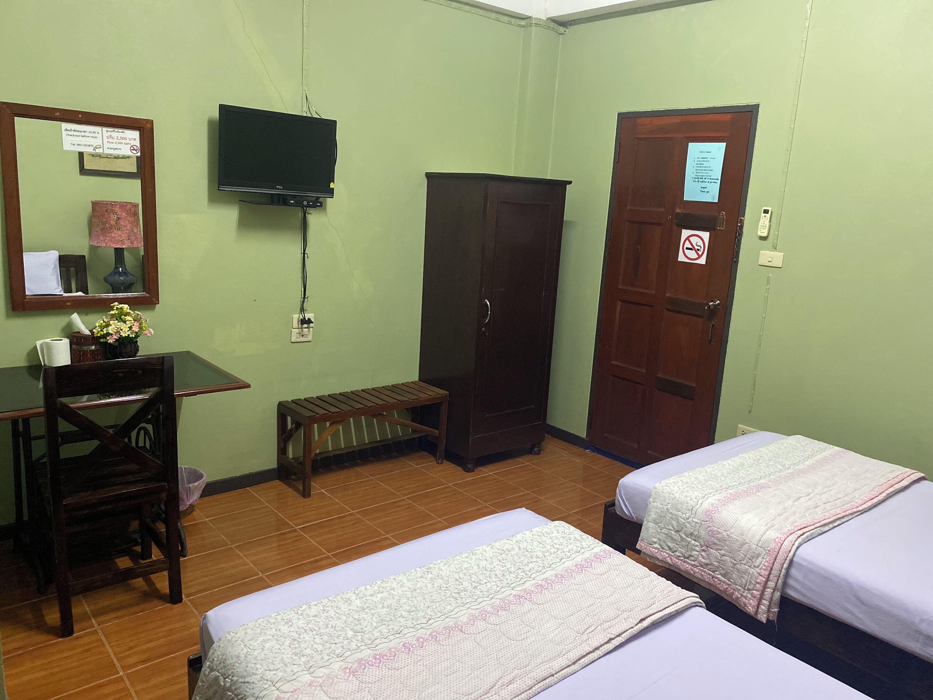 A room with two beds, a desk with a computer, a television, a wardrobe, and a door with a sign.