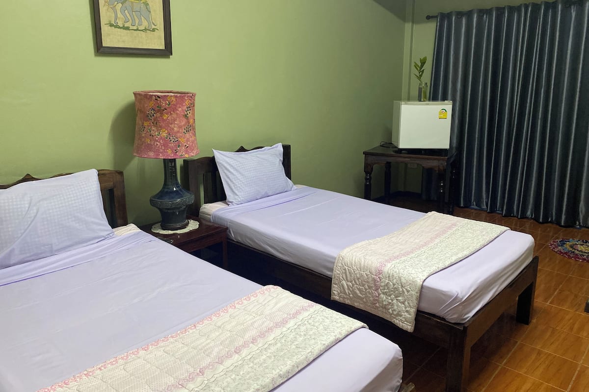 A room with two beds, a small table with a lamp, a TV, and a curtain.