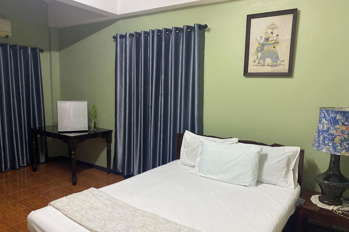 A hotel room with a bed, a small table with a lamp, a picture on the wall, and curtains.