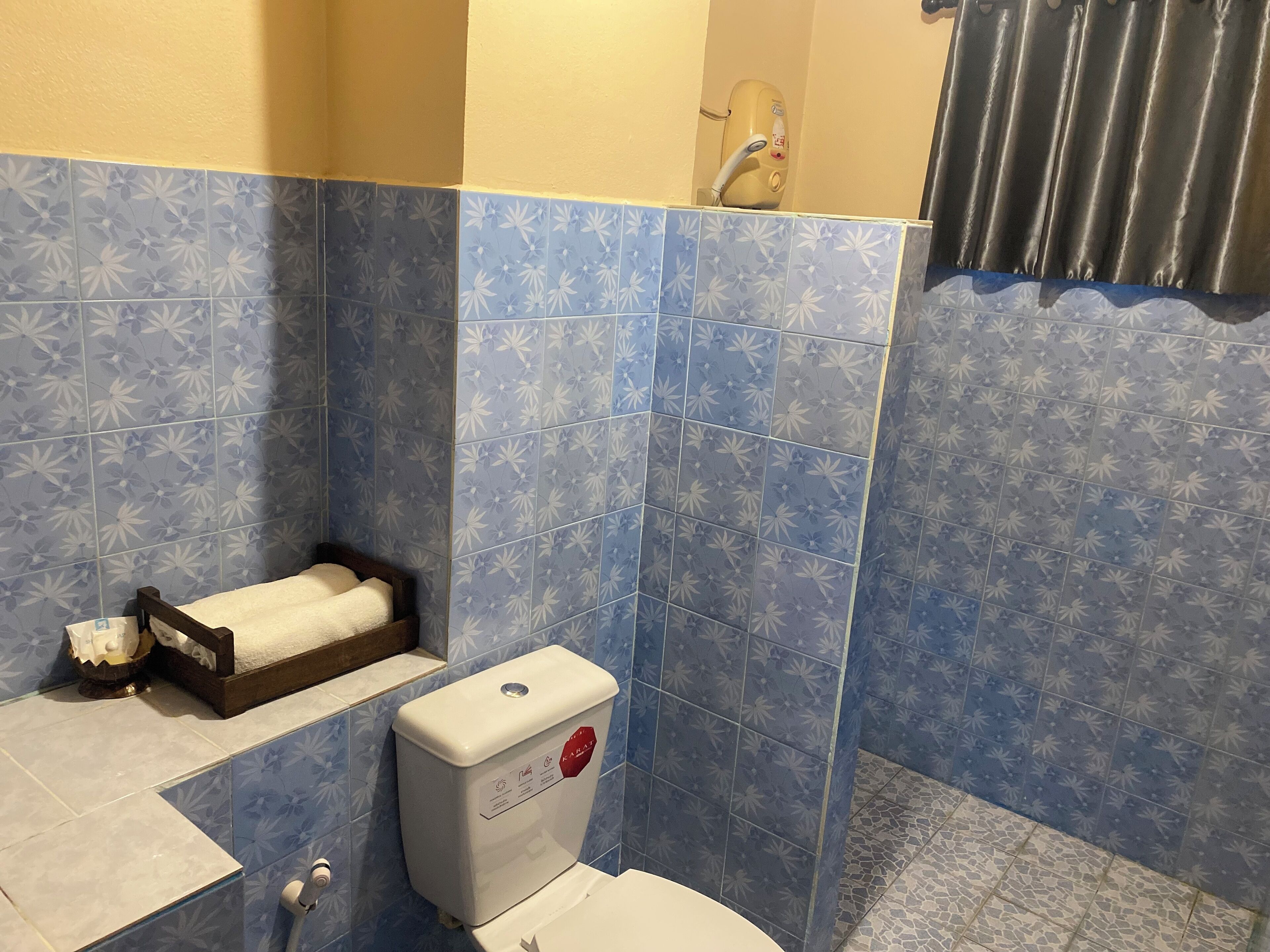 Ein Badezimmer mit blauen, floralen Fliesen, einer Toilette, einem Waschbecken mit Handtuch und einer Duschkabine.