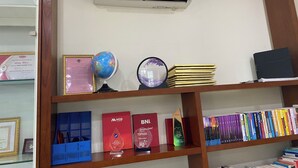 A room with a wooden shelf displaying books, a globe, framed certificates, and a wall-mounted air conditioner. -  MMG GLOBAL Apartments (Hai Phong)