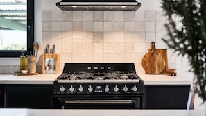 Uma cozinha com um fogão preto da SMEG, uma tábua de corte de madeira e um suporte para facas.