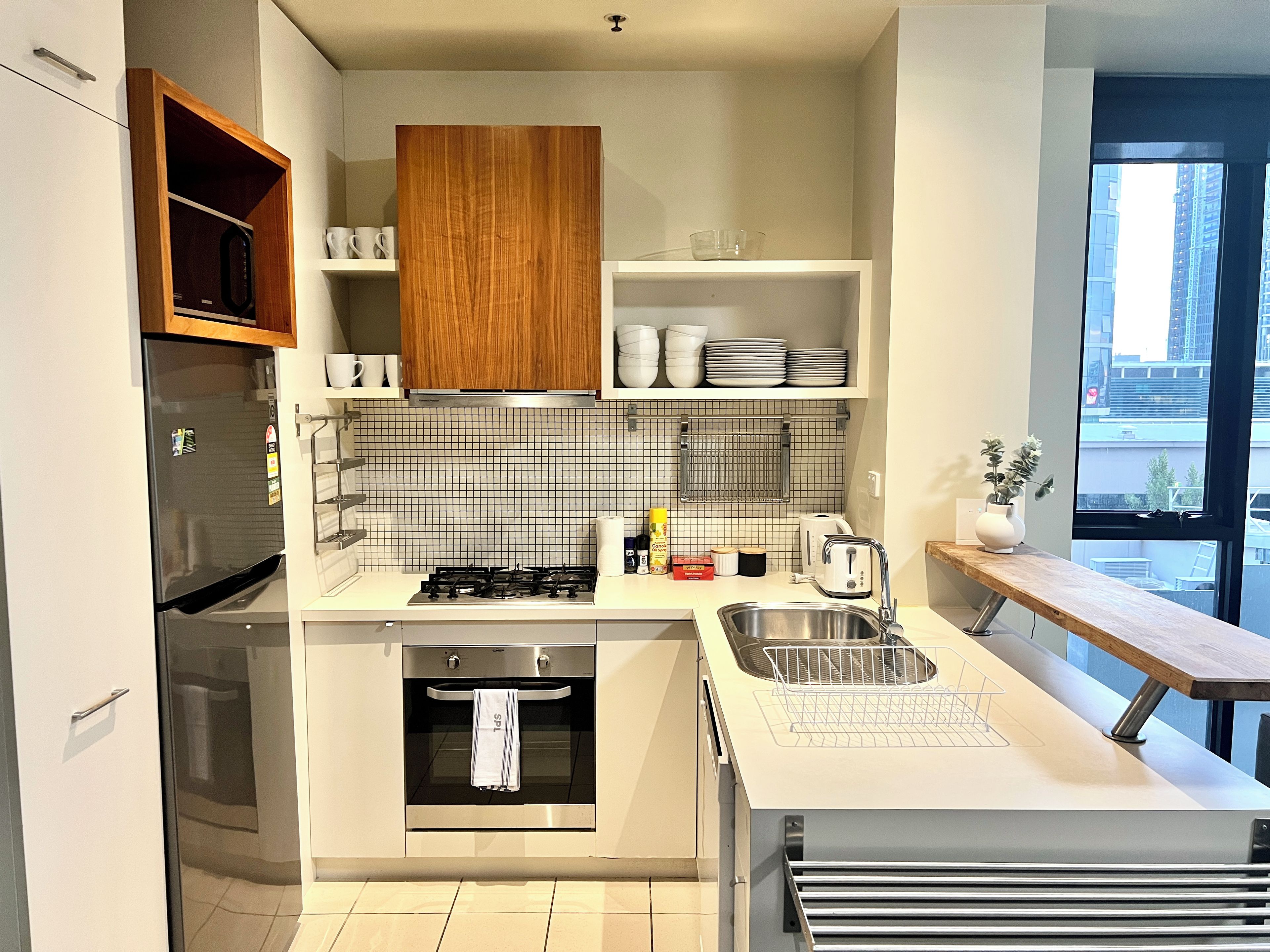 A modern kitchen with a built-in oven, a stainless steel sink, and a window overlooking a cityscape.