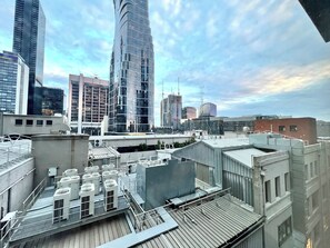 A rooftop with multiple air conditioning units, a metal staircase, and a view of surrounding high-rise buildings. - Readyset Apartments on Little Bourke (Melbourne)