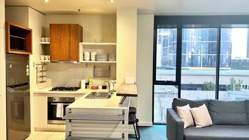 Una cocina moderna con refrigerador, estufa y lavamanos, además de un espacio de sala con sofá y ventanas amplias.