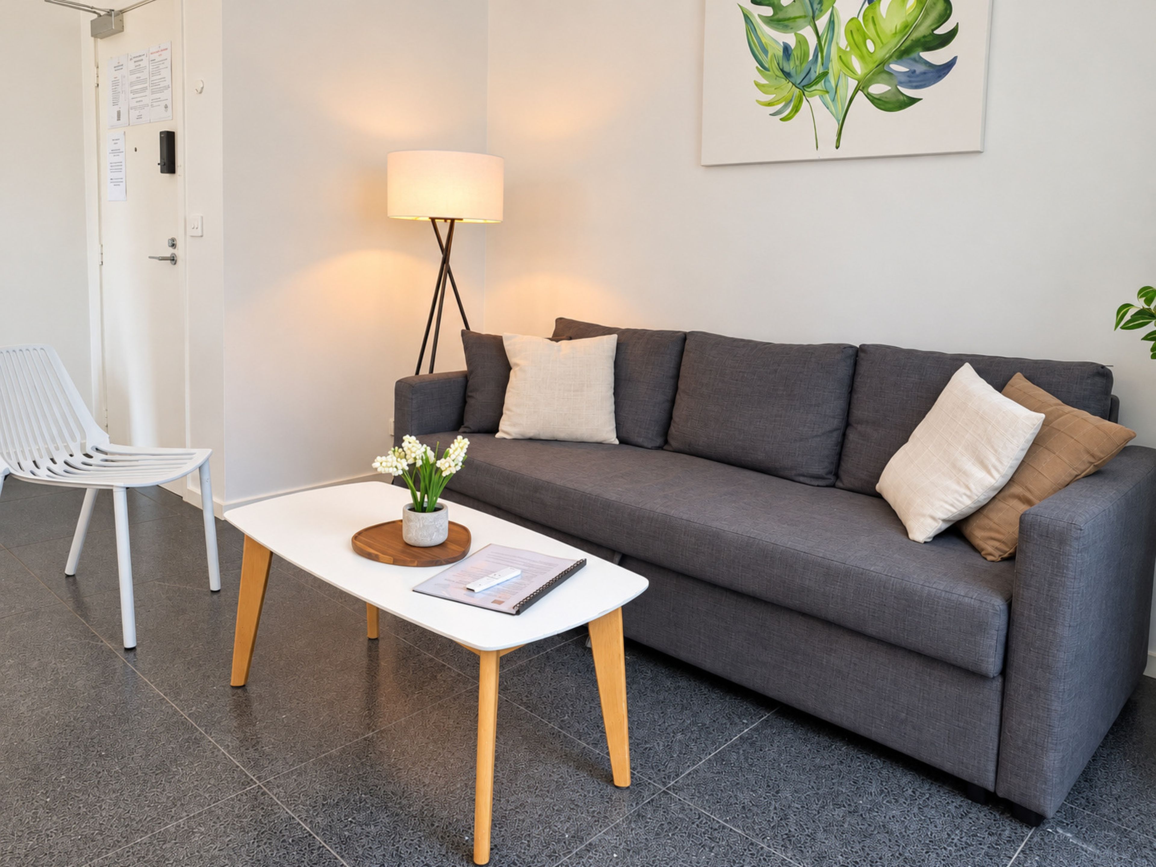 Una sala de estar moderna con un sofá gris, una silla blanca, una mesita con un jarrón de flores y una lámpara de pie.