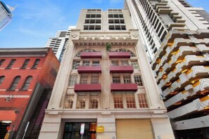 A multi-story building with a central entrance, large windows, and a series of balconies on the upper floors. - Readyset Apartments on Little Bourke (Melbourne)