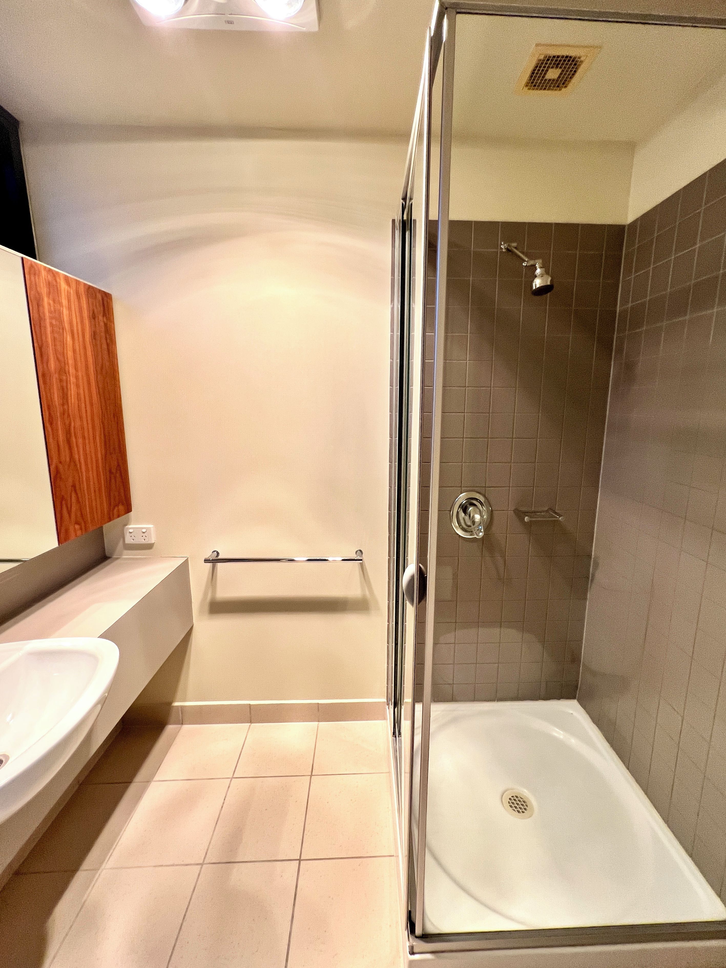 A modern bathroom with a glass-enclosed shower, a white sink, and a wooden vanity.
