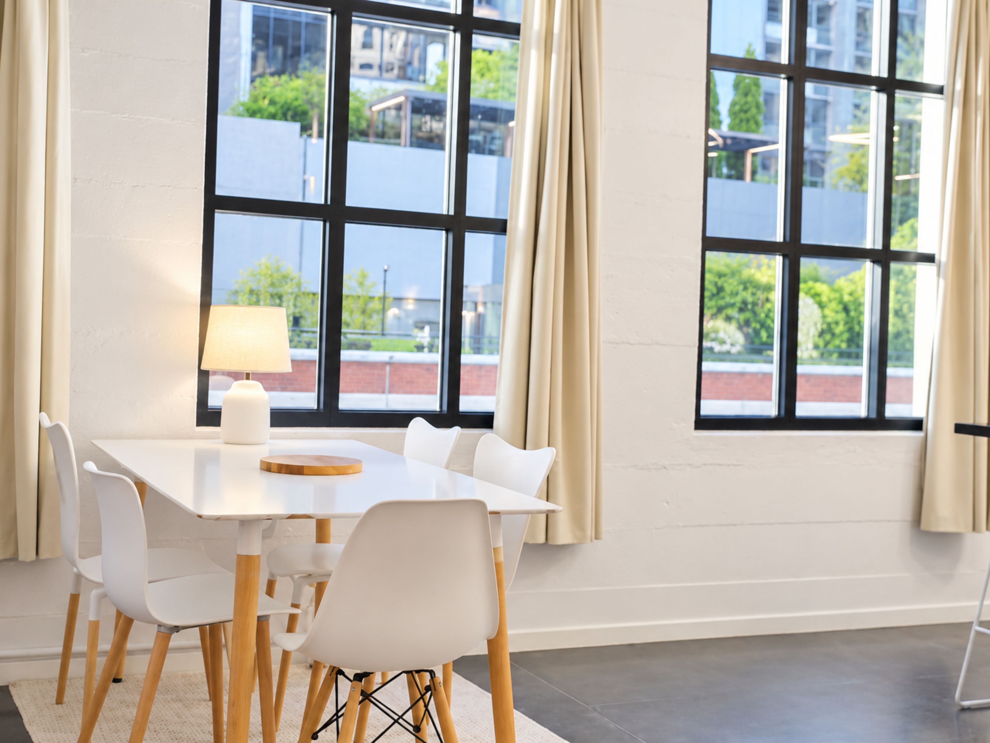 A modern hotel room with a large window, a white table, and four chairs.