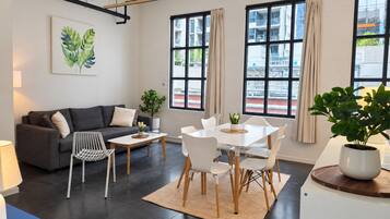 Una sala de estar moderna con un sofá, mesa de comedor, sillas y una mesa de centro. Hay una planta en maceta sobre la mesa y otra en un pedestal.