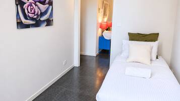 A hotel room with a bed, a painting on the wall, and a nightstand with a lamp.