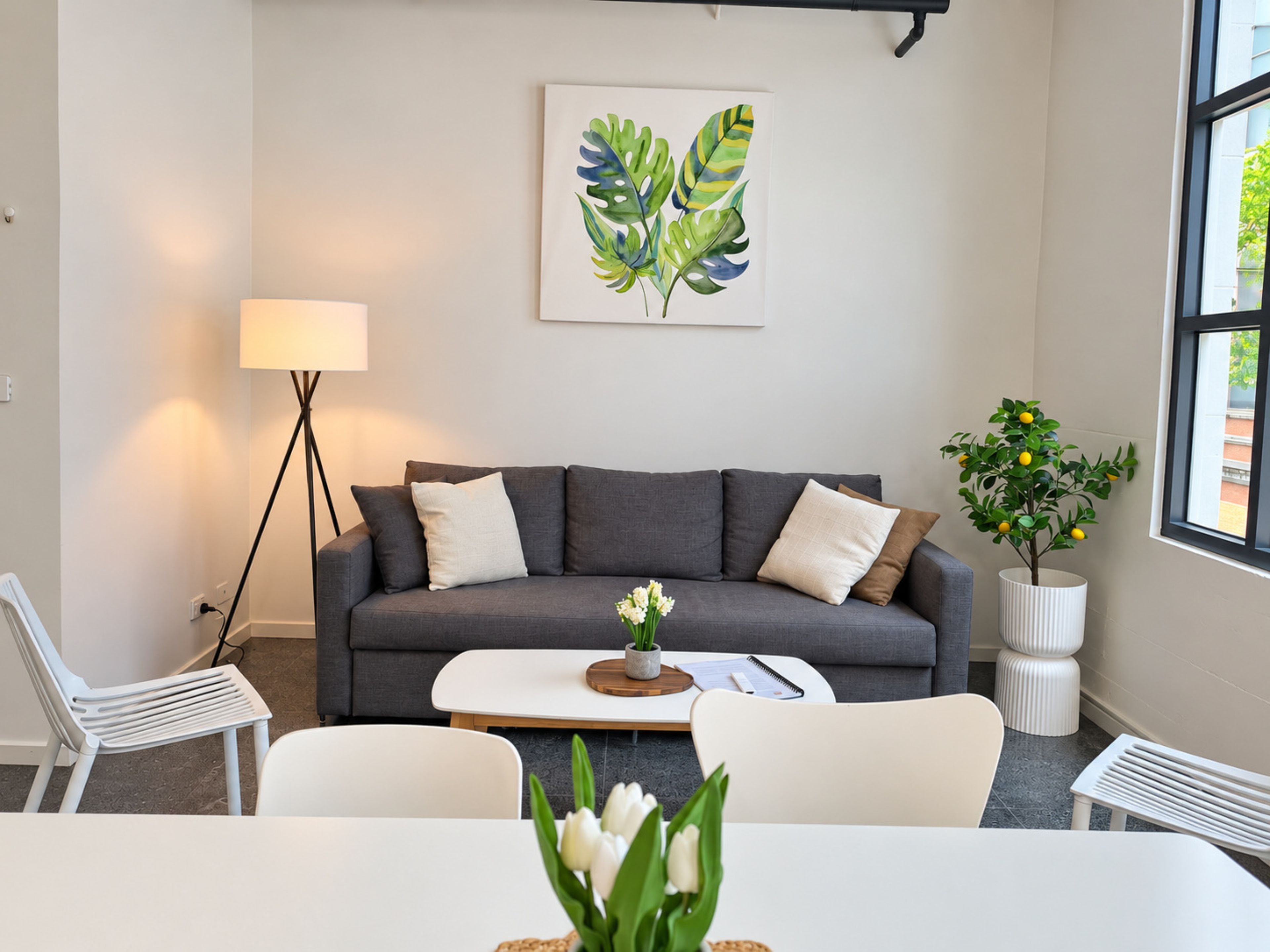 Una sala de estar moderna con un sofá gris, sillas blancas, una mesa de centro, una lámpara y una planta en maceta.