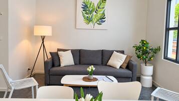 Una sala de estar moderna con un sofá gris, sillas blancas, una mesa de centro, una lámpara y una planta en maceta.