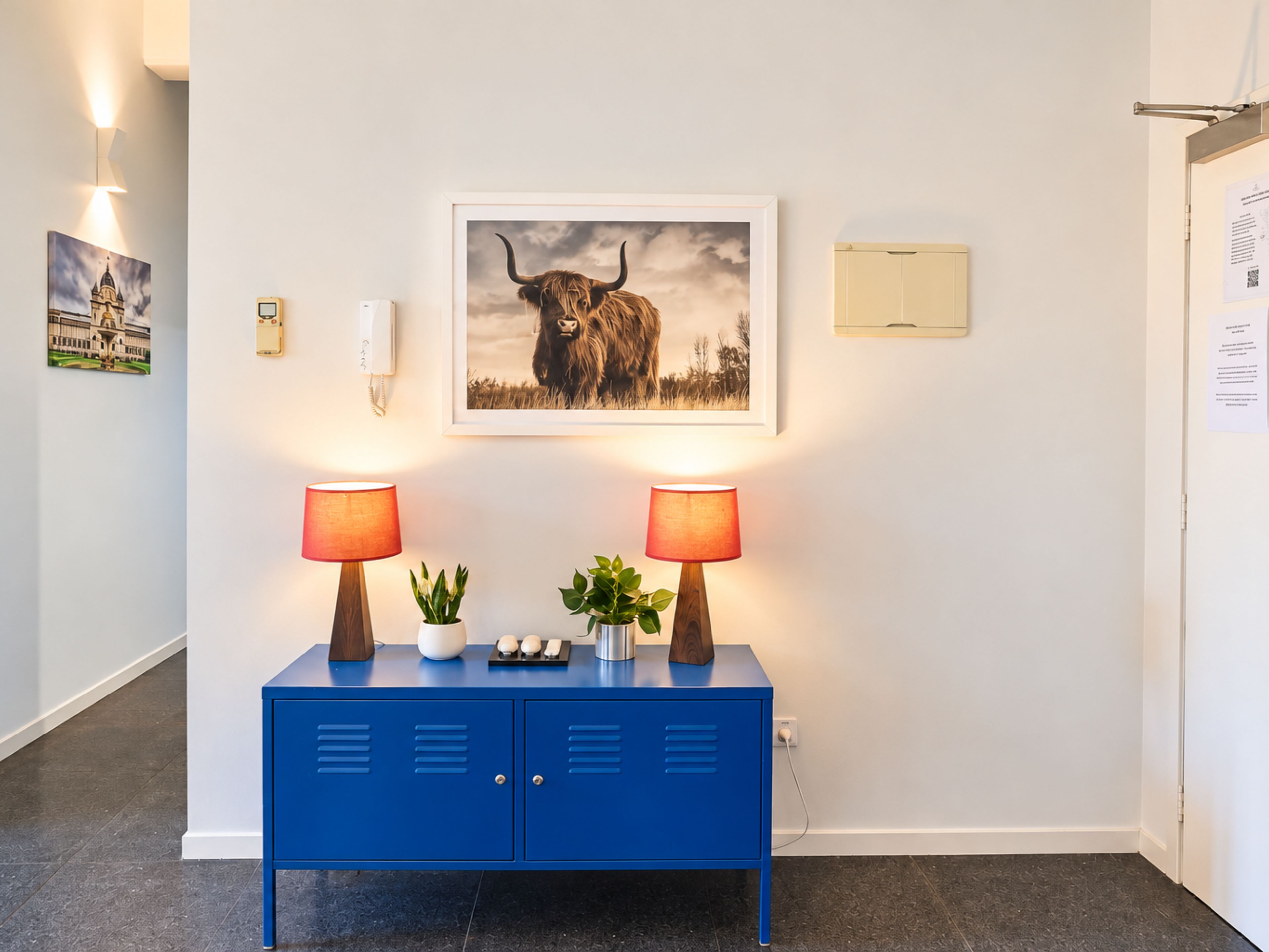 A blue cabinet with two lamps, a framed picture of a bull, and a small plant.