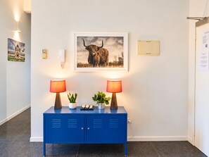 A blue cabinet with two lamps, a framed picture of a bull, and a small plant.