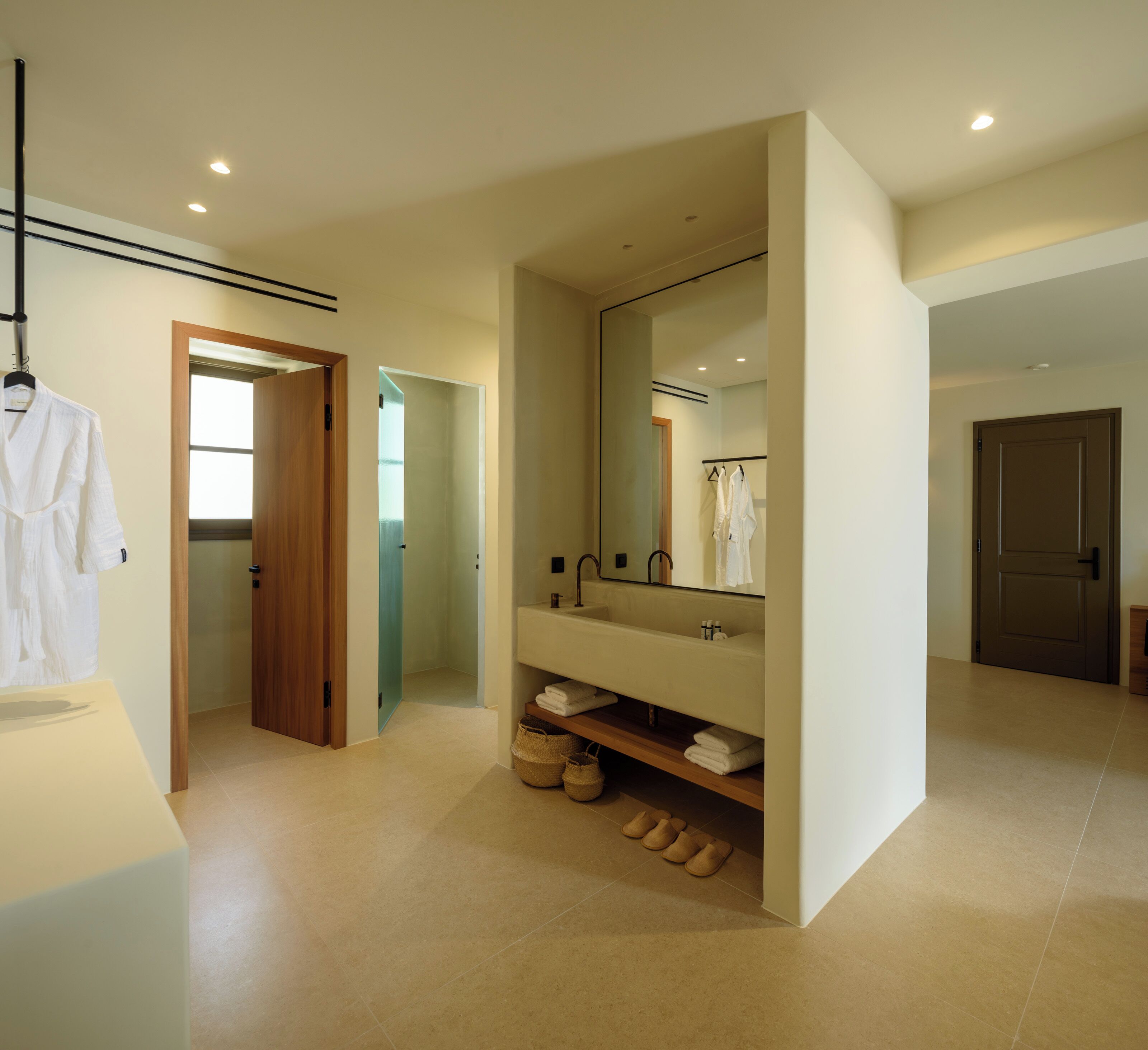 Une salle de bain moderne avec un grand miroir, un lavabo et un porte-serviettes. Une porte en bois donne accès à une autre pièce.