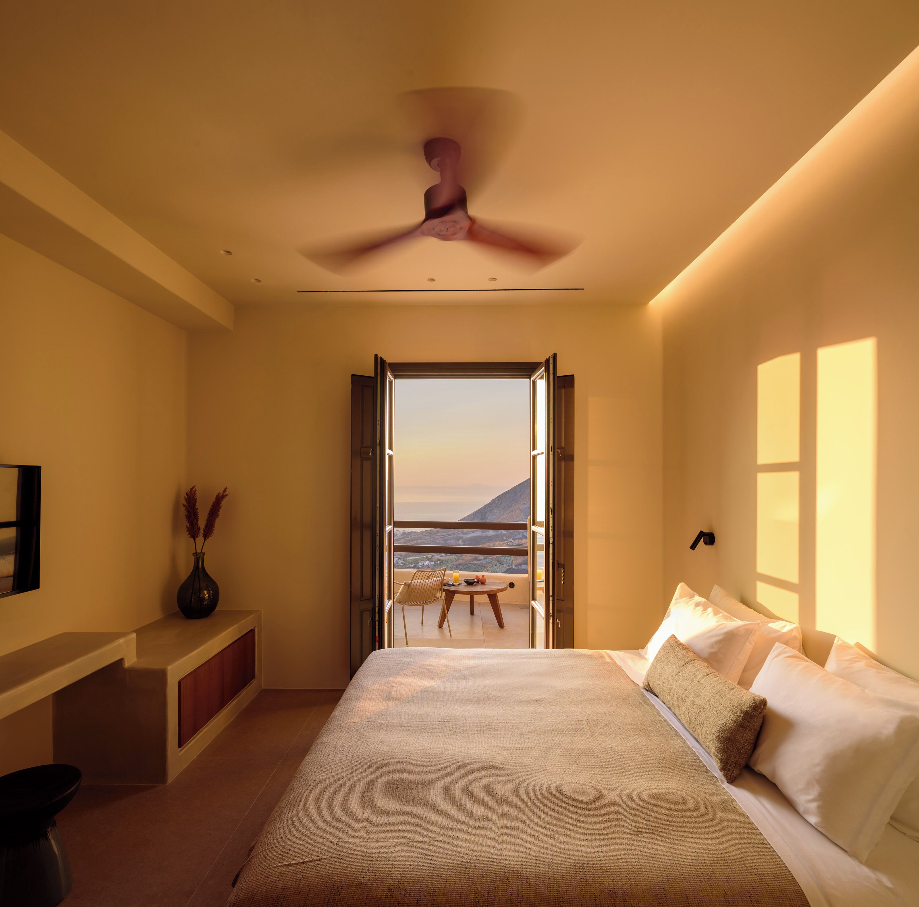 A bedroom with a bed, a desk, a chair, and a view of the sea.