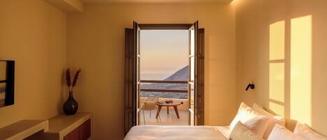 A bedroom with a bed, a desk, a chair, and a view of the sea.