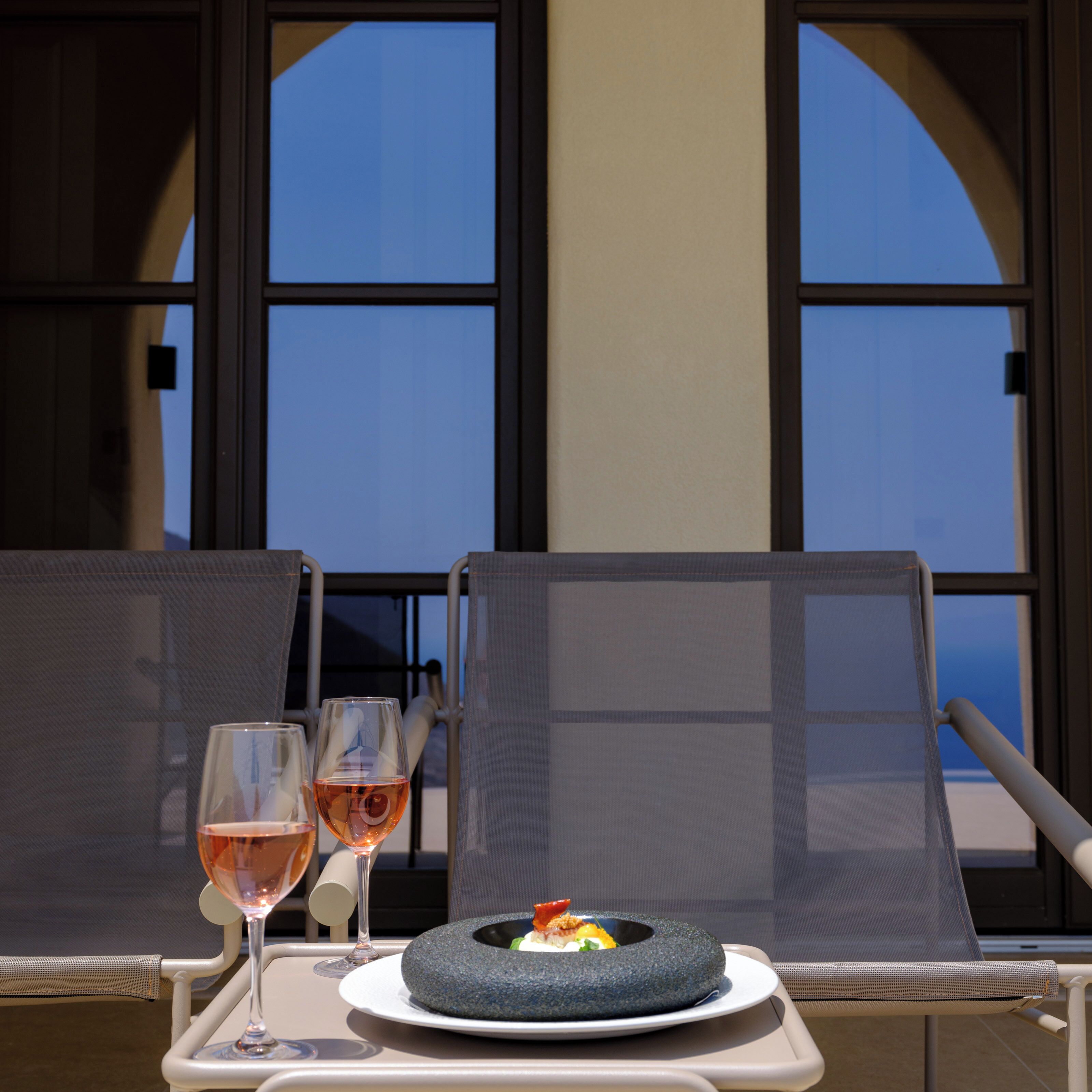 A dining table with two chairs, a plate of food, and two glasses of wine.