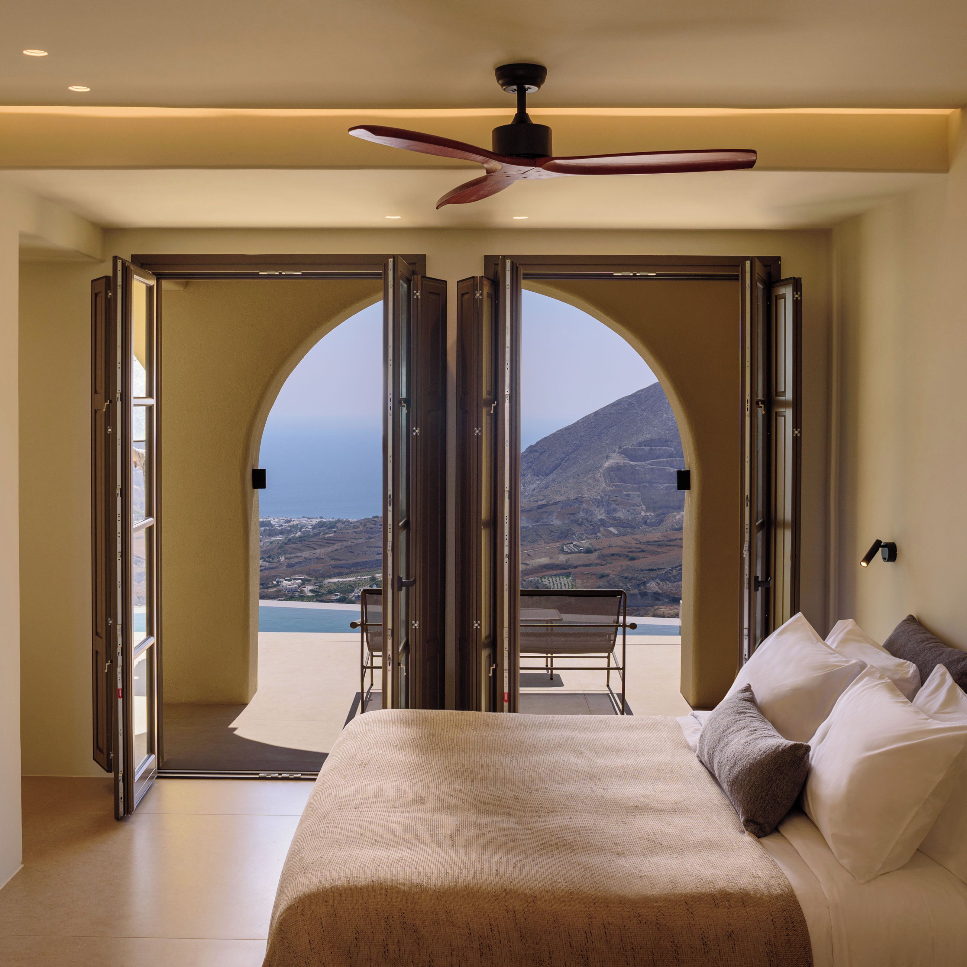 A bedroom with a bed, pillows, and a view of a mountainous landscape through open doors.