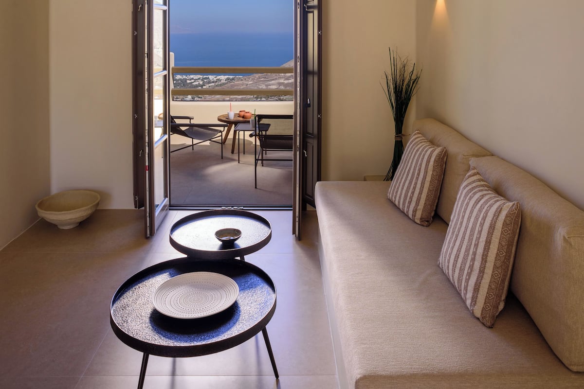 A modern living room with a sofa, a small round table, and a view of the sea through an open door.