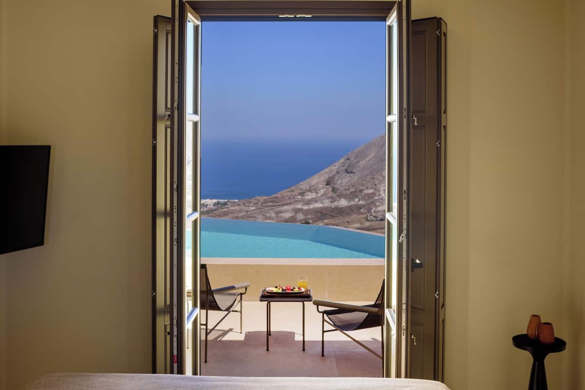 A bedroom with a bed, a ceiling fan, and an open door leading to a balcony with a view of the sea.