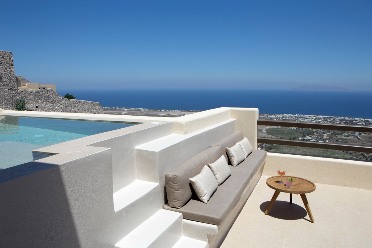 A poolside area with a white sofa and a small round table, overlooking a coastal landscape.