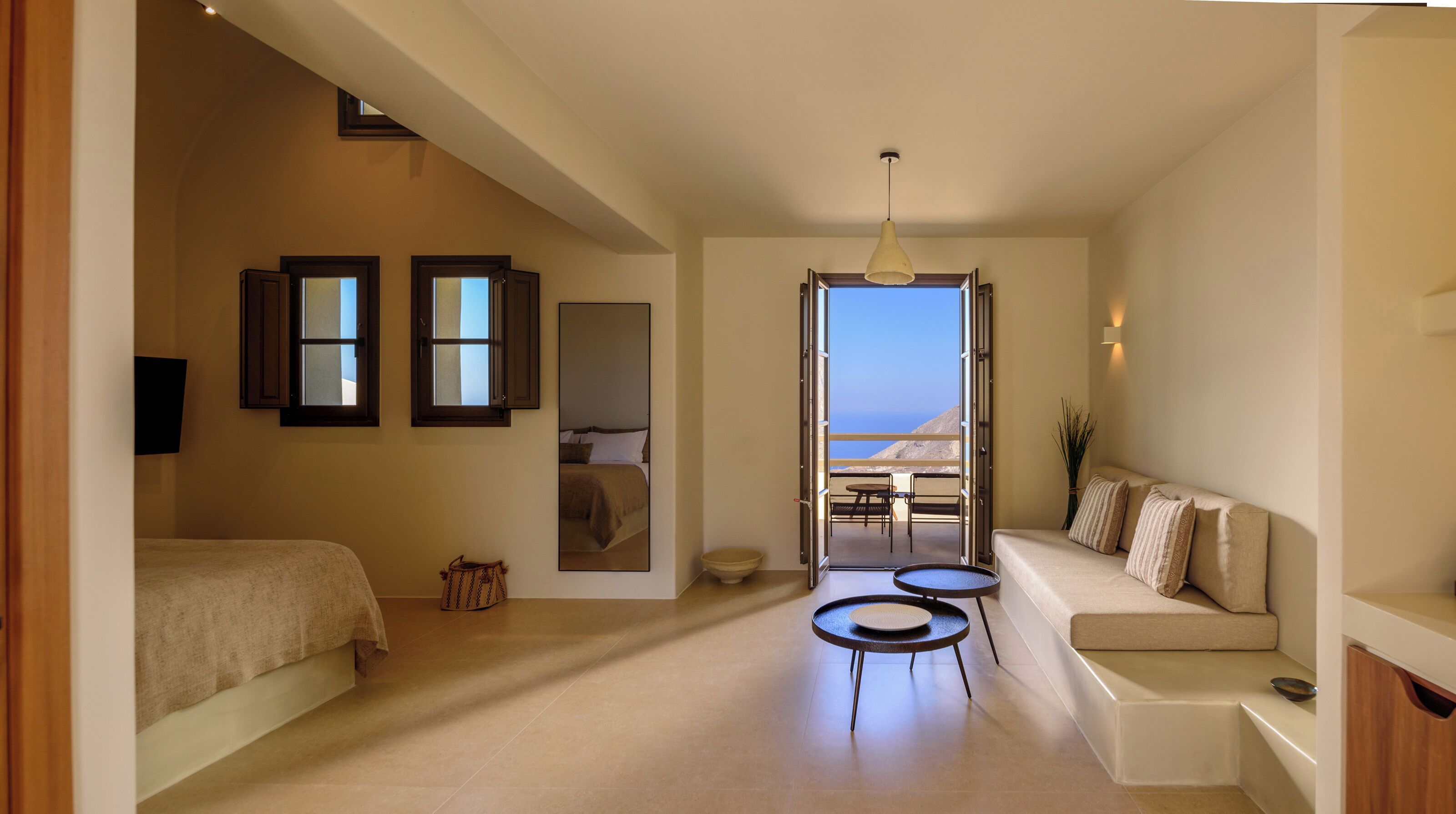 A hotel room with a bed, a sofa, a small table, and a view of the sea.