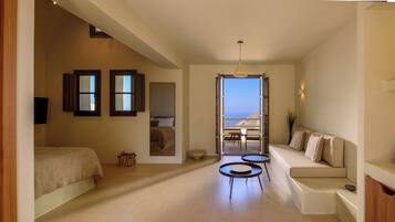 A hotel room with a bed, a sofa, a small table, and a view of the sea.